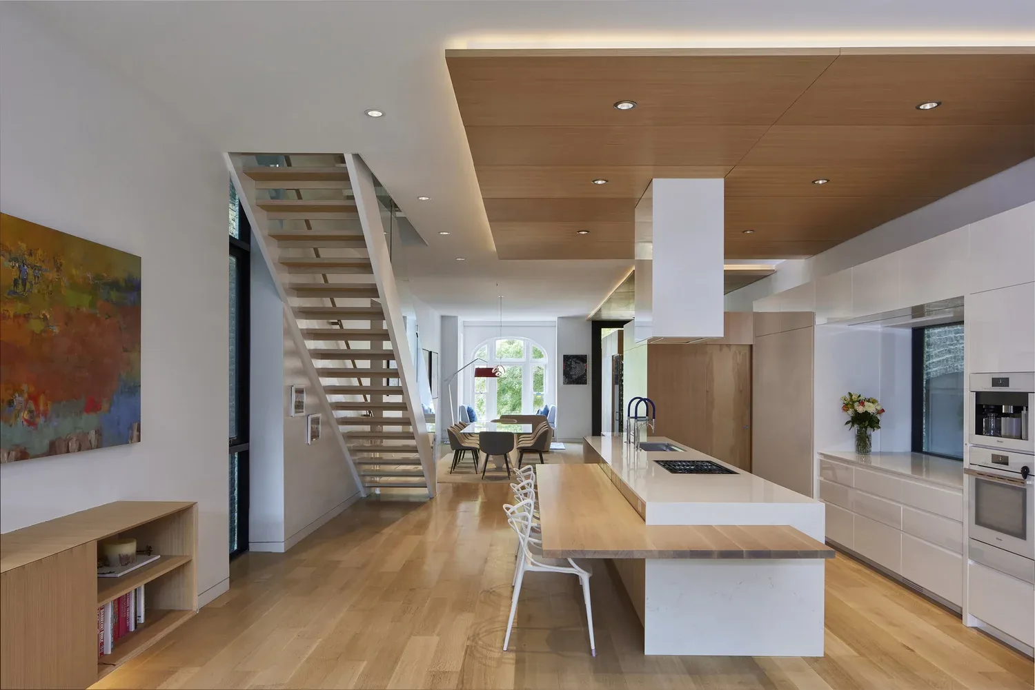 Interior view of a modern kitchen and dining area featuring a wood ceiling panel, a staircase with open risers, and integrated kitchen appliances.