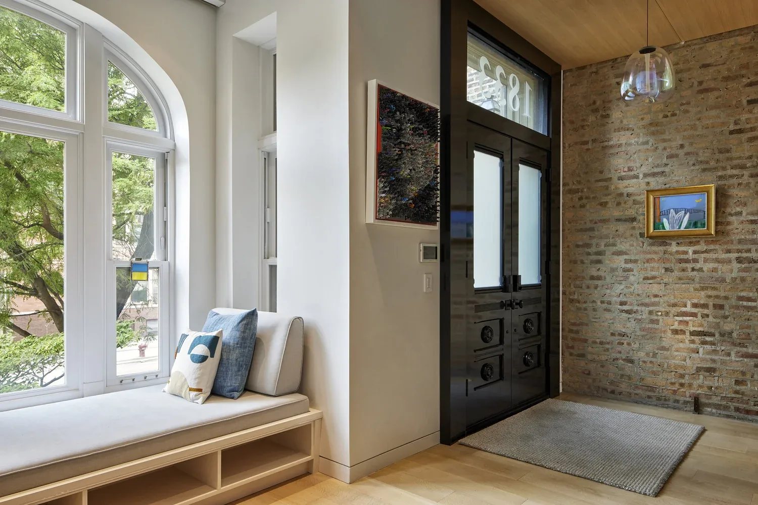 Entry area with a bench by arched windows, black double entry doors, and an exposed brick accent wall.