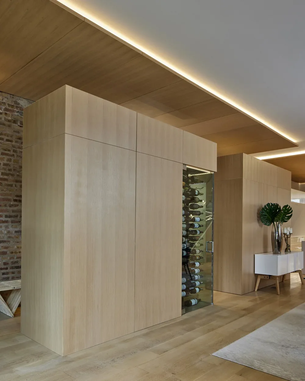 Wine storage with glass door integrated into light wood paneling in a modern interior space.