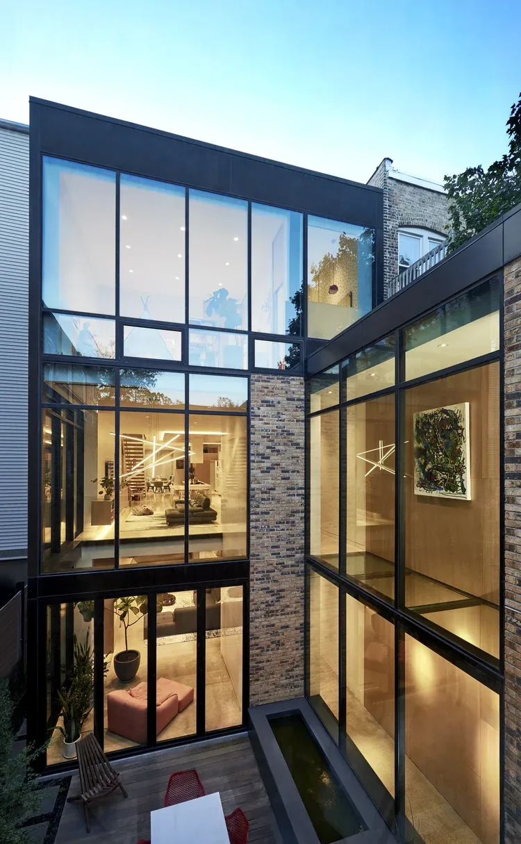 The rear facade of the house includes extensive floor-to-ceiling glazing and a brick column separating glass sections.