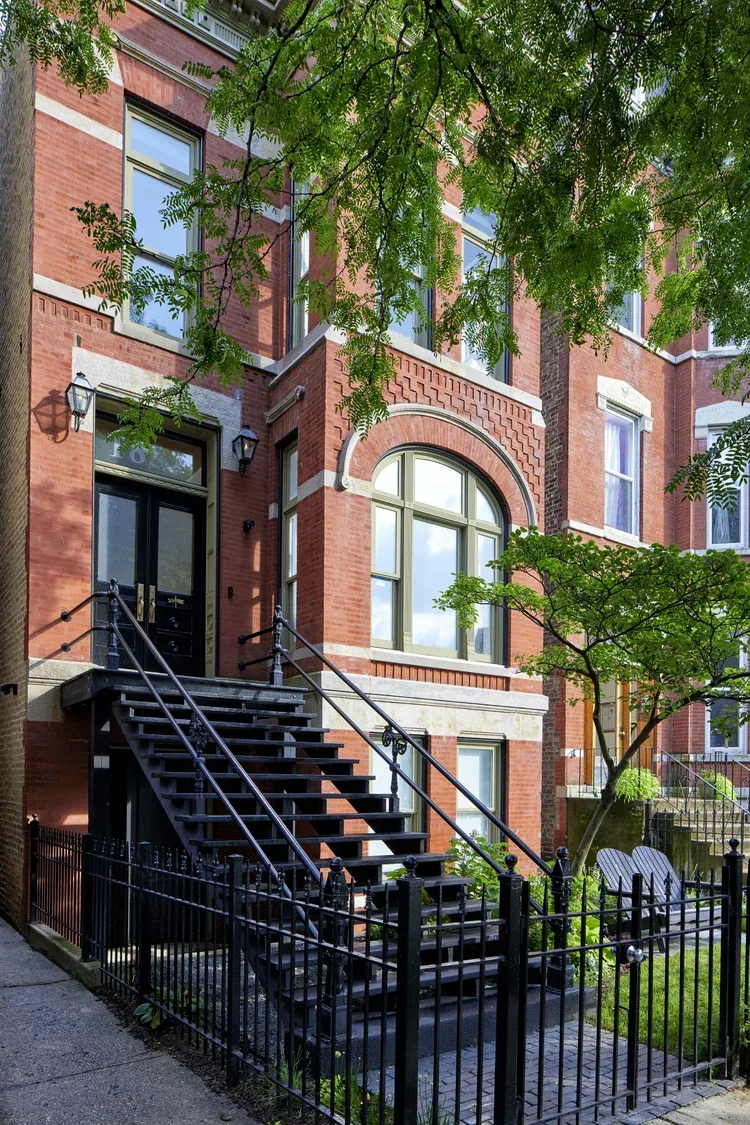 Front exterior of a red brick residential building featuring black metal stairs, black door, and large windows framed with stone lintels.