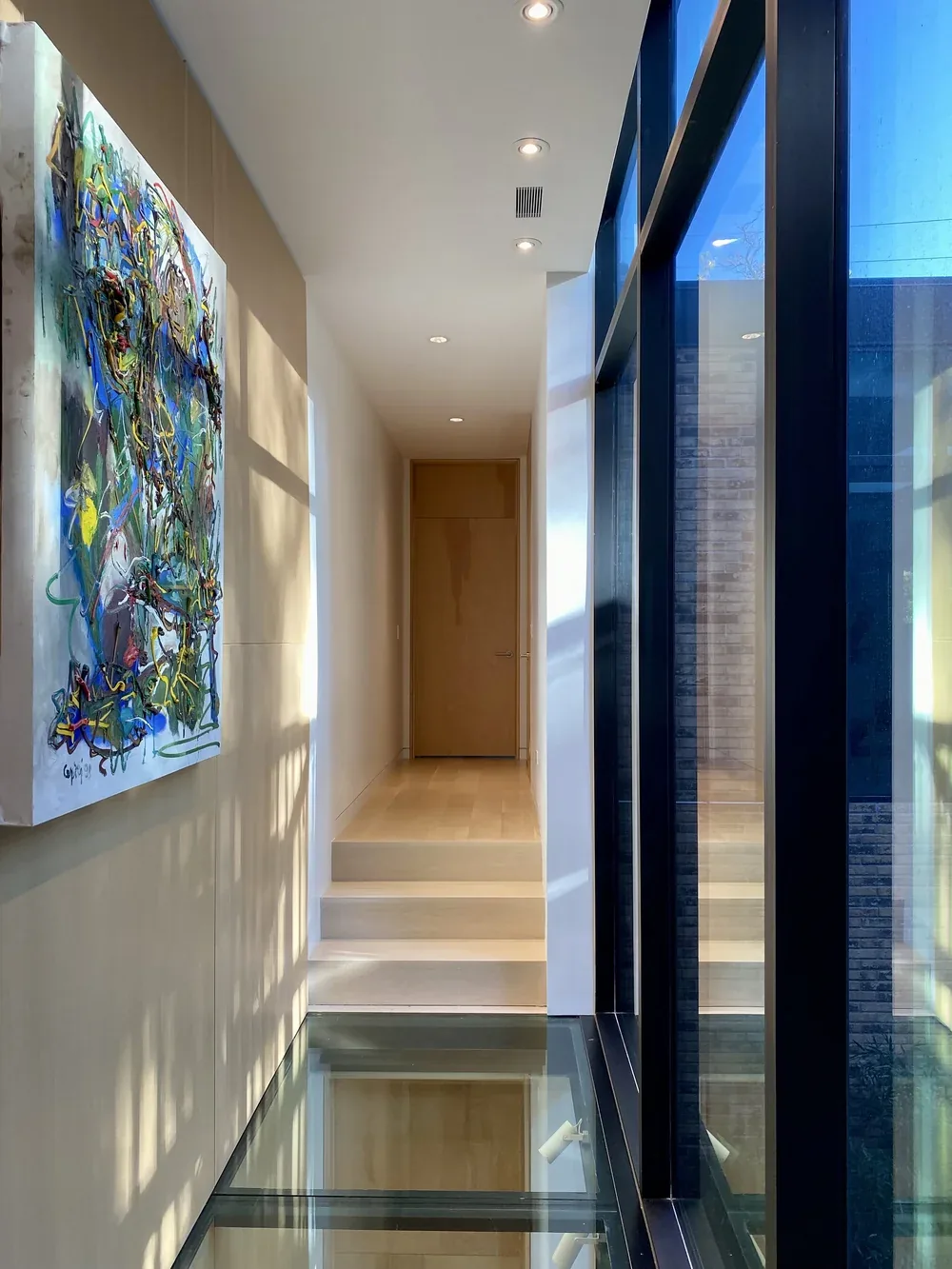 Hallway with glass floor panel, wood door, recessed lighting, and floor-to-ceiling windows on right