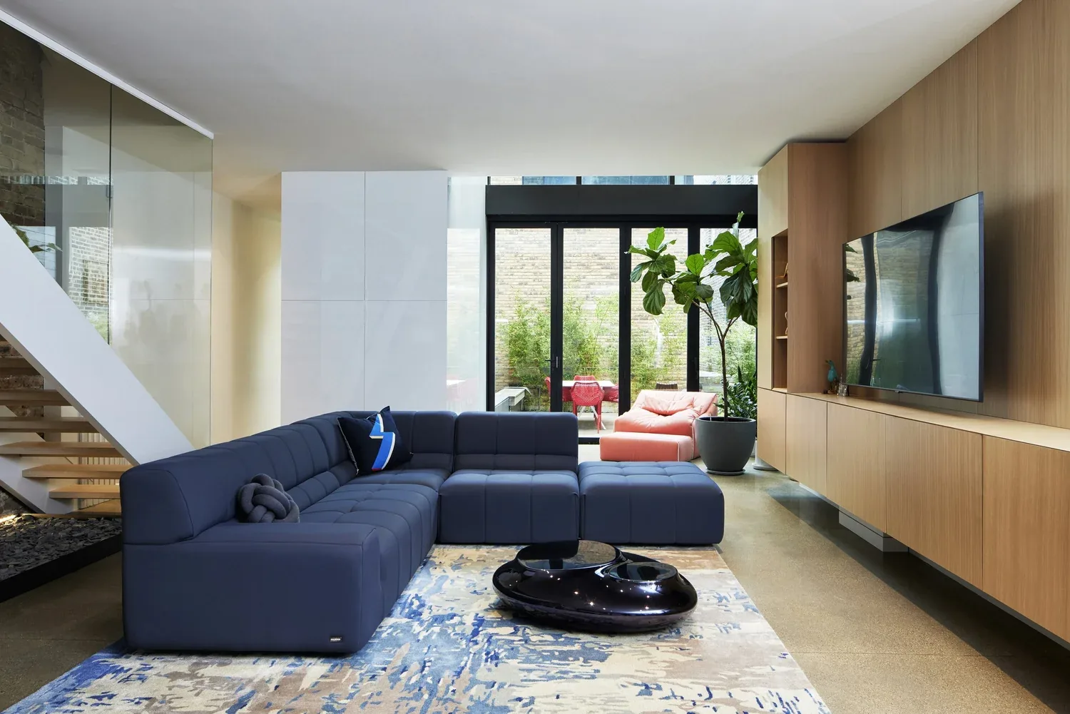 Interior view of a modern living room with floor-to-ceiling black framed sliding glass doors opening to a patio.