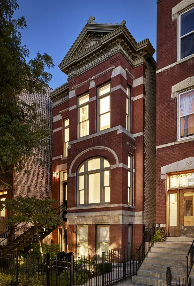 Front facade of a red brick townhouse with large rectangular and arched windows accented by white stone bands and cornice detailing.