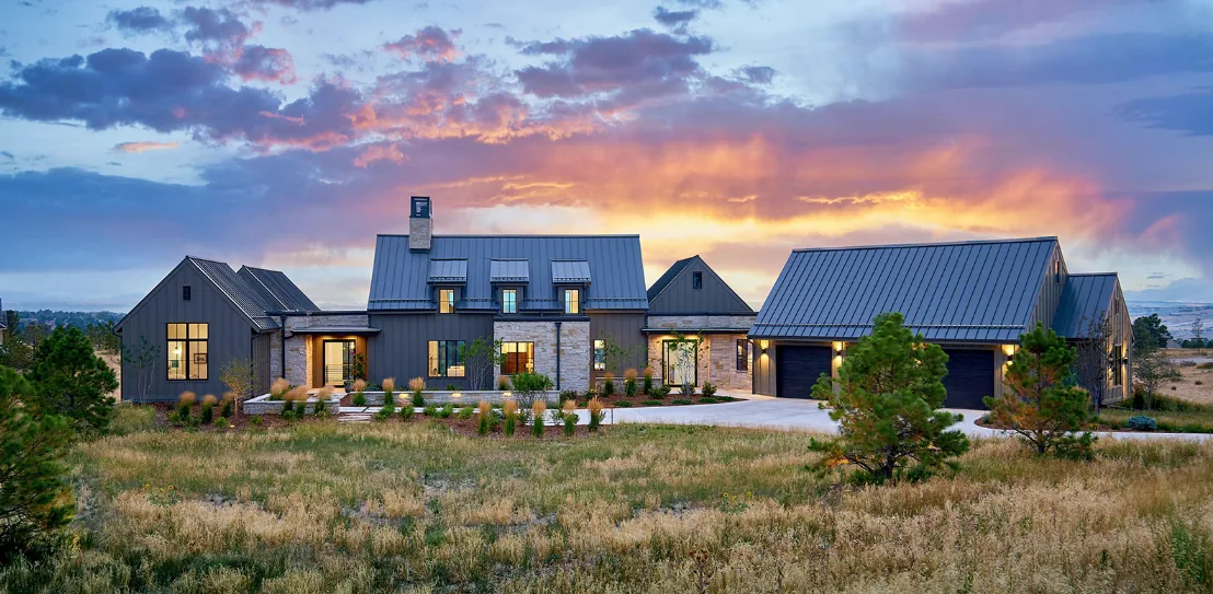 Contemporary farmhouse with metal standing seam roofs, black window frames, and stone chimney stack.