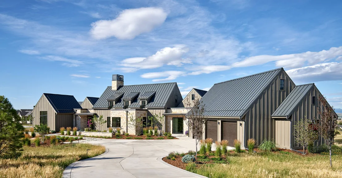 Contemporary farmhouse featuring multiple gable roofs, stone and vertical siding, metal roof, and covered patios in a rural setting.