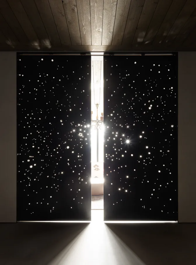 Black double doors with a starry pattern allow bright light to filter into a dim space.