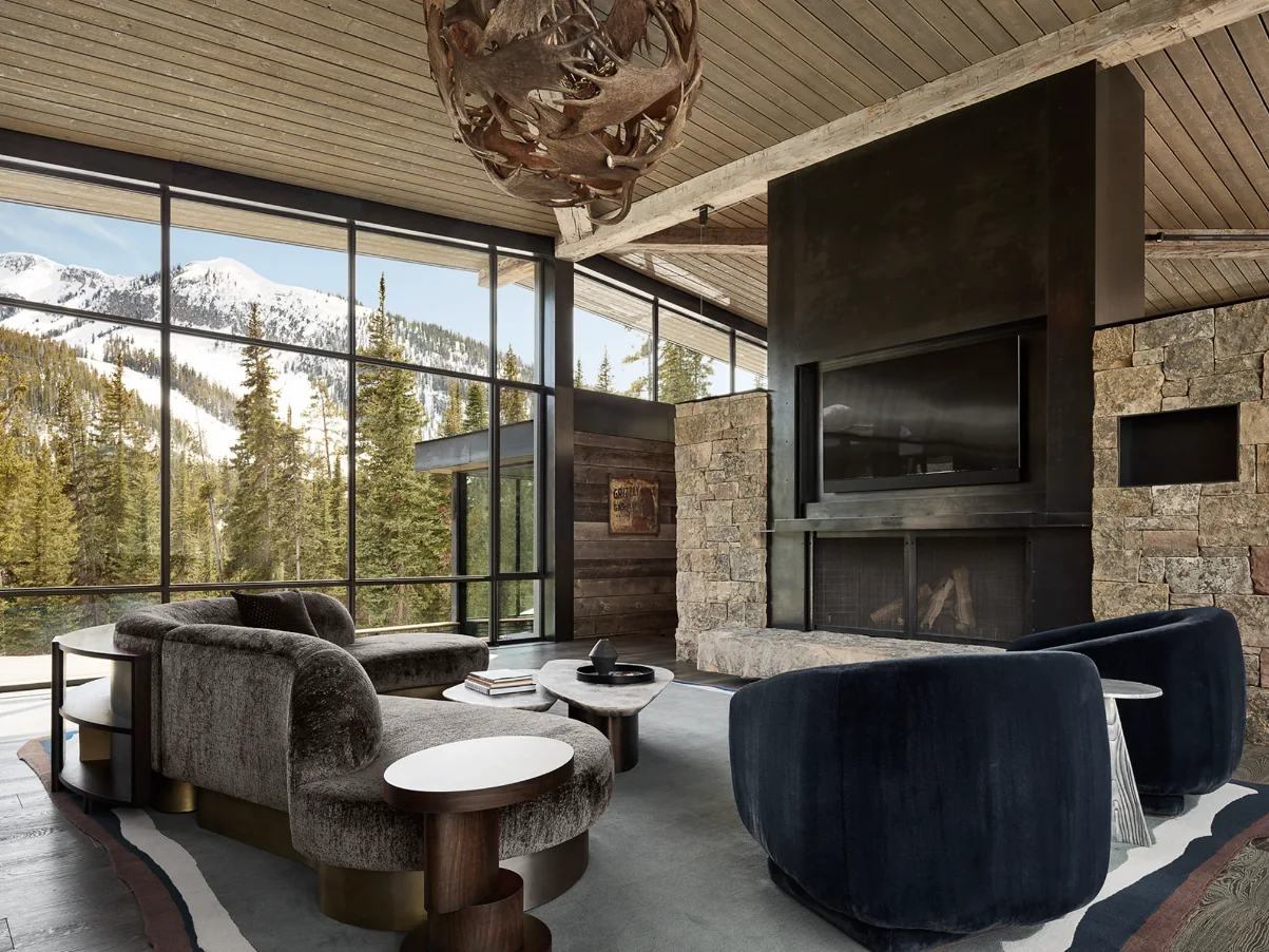 Living room with panoramic glass walls revealing a mountain view and a stone fireplace with a mounted TV.