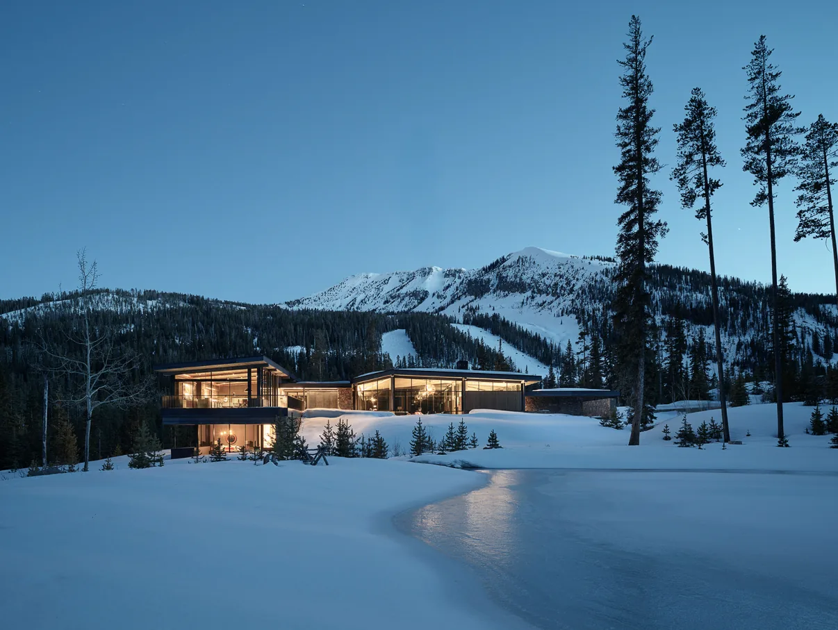 Contemporary home in a snowy mountain landscape with extensive floor-to-ceiling glazing showcasing interior warmth.