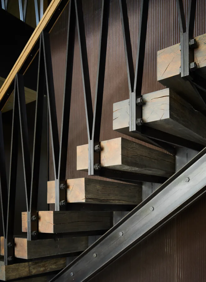Staircase featuring dark wooden steps supported by black metal braces and vertical rods.