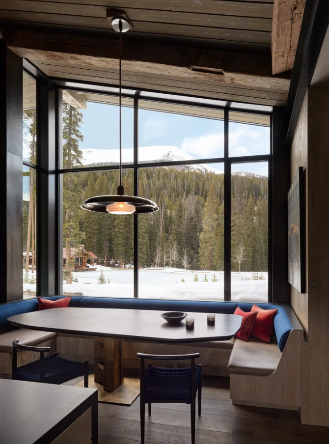 Dining nook in the YELLOWSTONE project by John Maniscalco Architecture with panoramic black metal window frames overlooking a snowy mountain landscape.