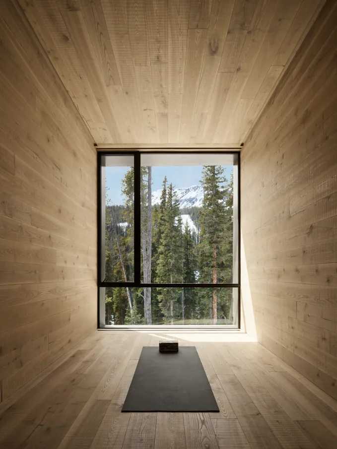 A serene wood-paneled room with floor-to-ceiling window framing snowy pines and mountain views.