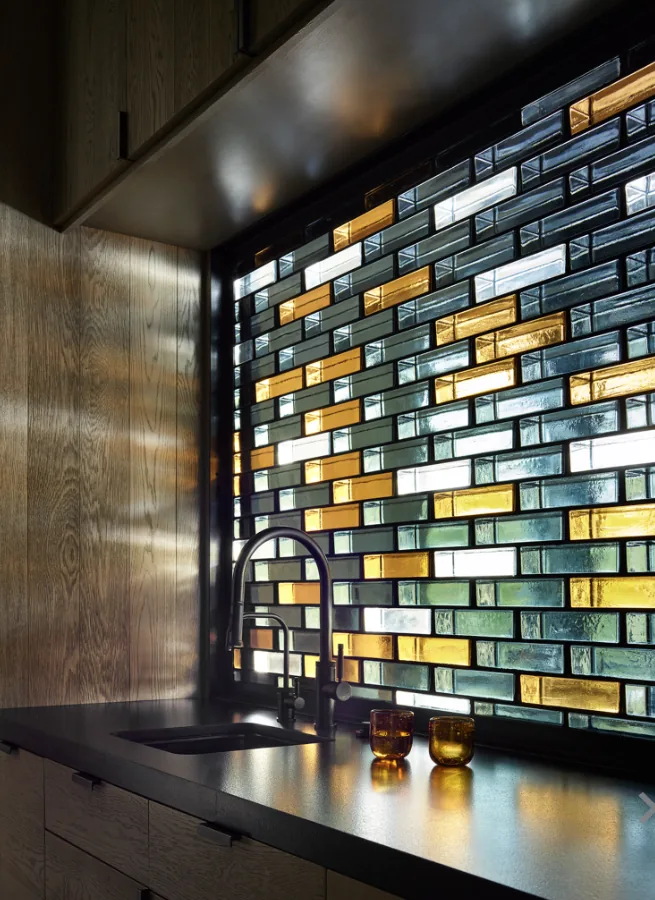 Kitchen sink in front of a decorative mosaic glass window with warm wood cabinetry.