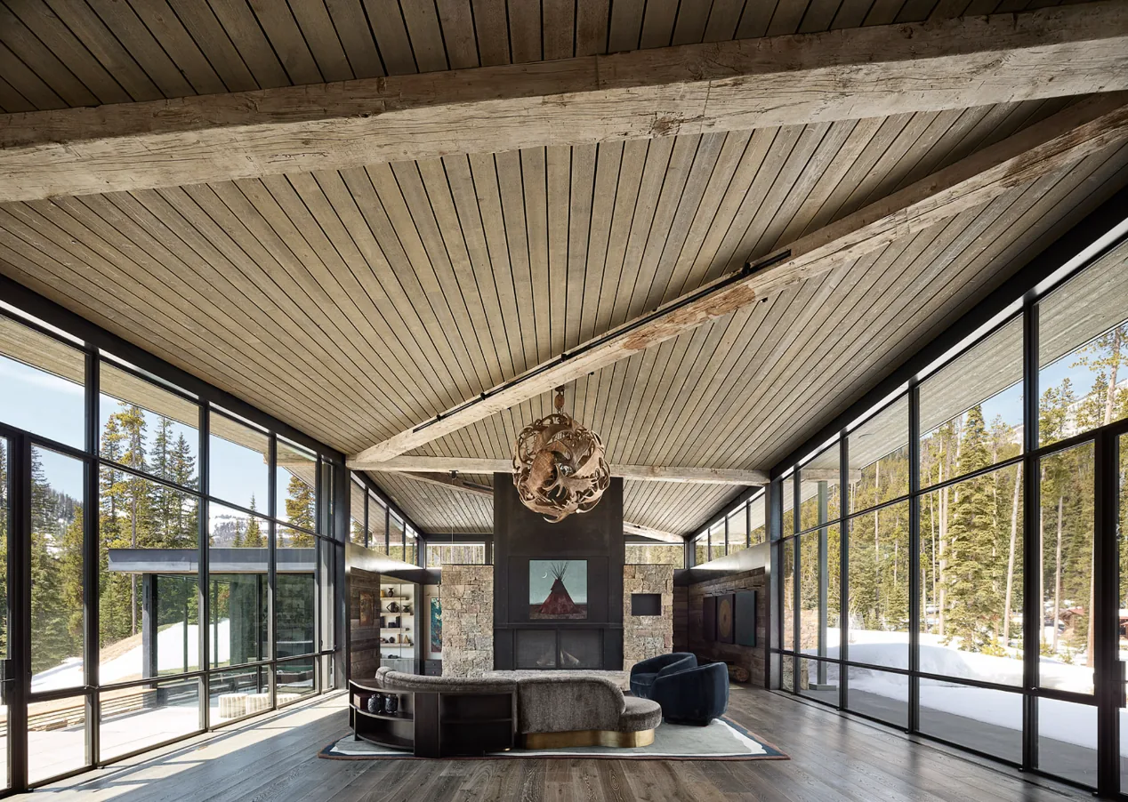 Living room features floor-to-ceiling glazing with black window frames, a stone fireplace, and exposed wood beams on the ceiling.