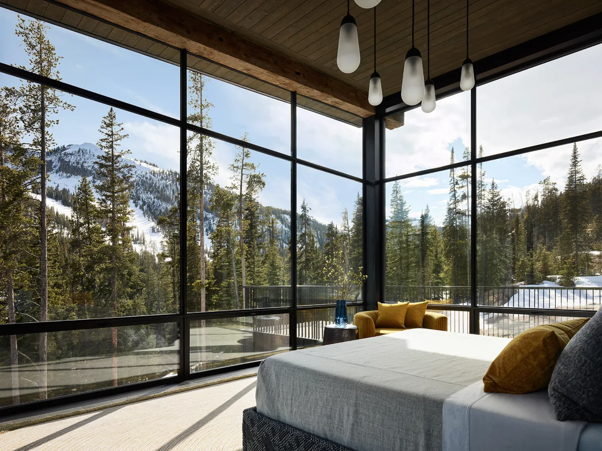 The bedroom features black metal window frames with a corner window providing expansive views of a snowy mountain and forest.