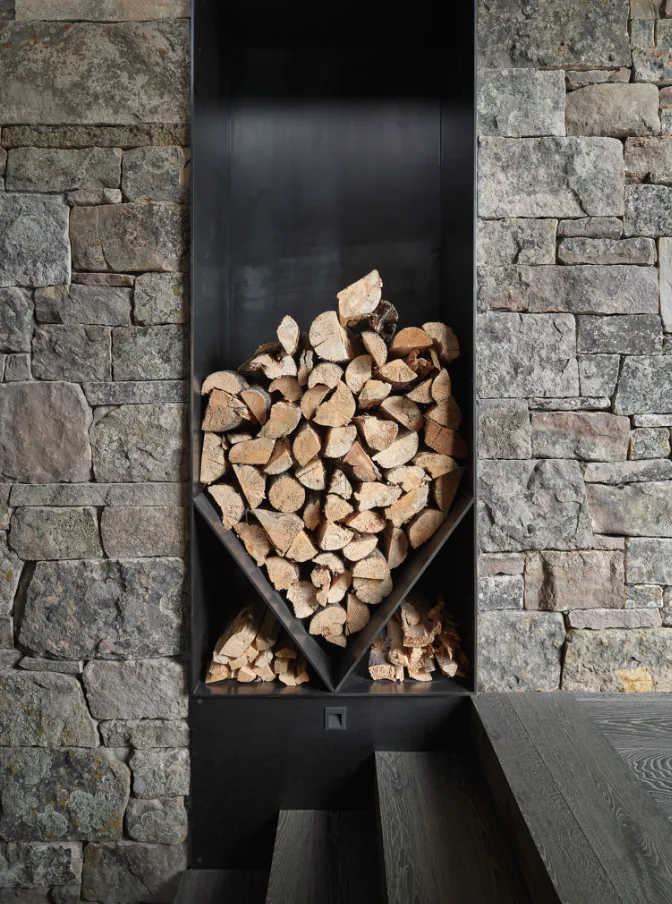 Firewood storage integrated into a metal wall niche surrounded by textured stone and adjacent to dark wood stairs.