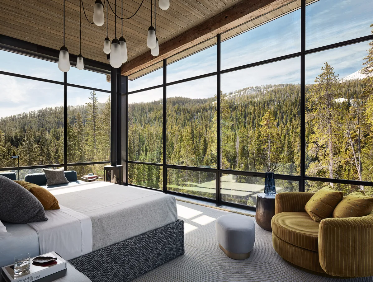 Bedroom features floor-to-ceiling glazing with views of a forested mountain landscape and a cozy sitting area.