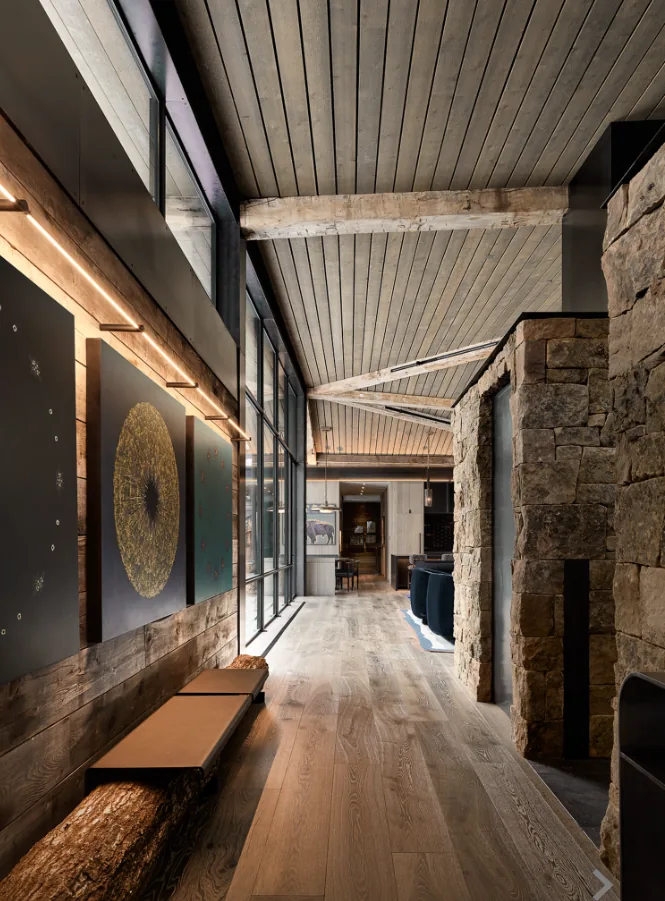 Interior hallway features textured stone walls, wood ceiling with beams, and large windows lighting the space.