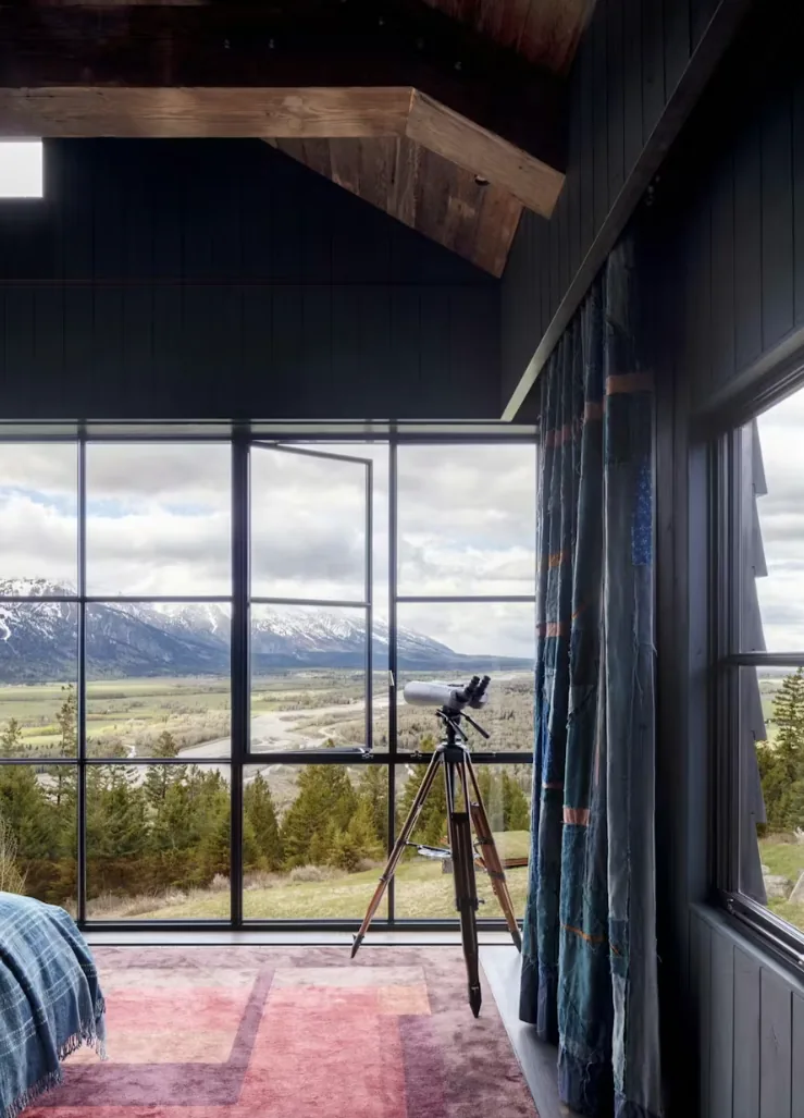 Room with floor-to-ceiling glazing offering mountain views and a tripod telescope by the window.