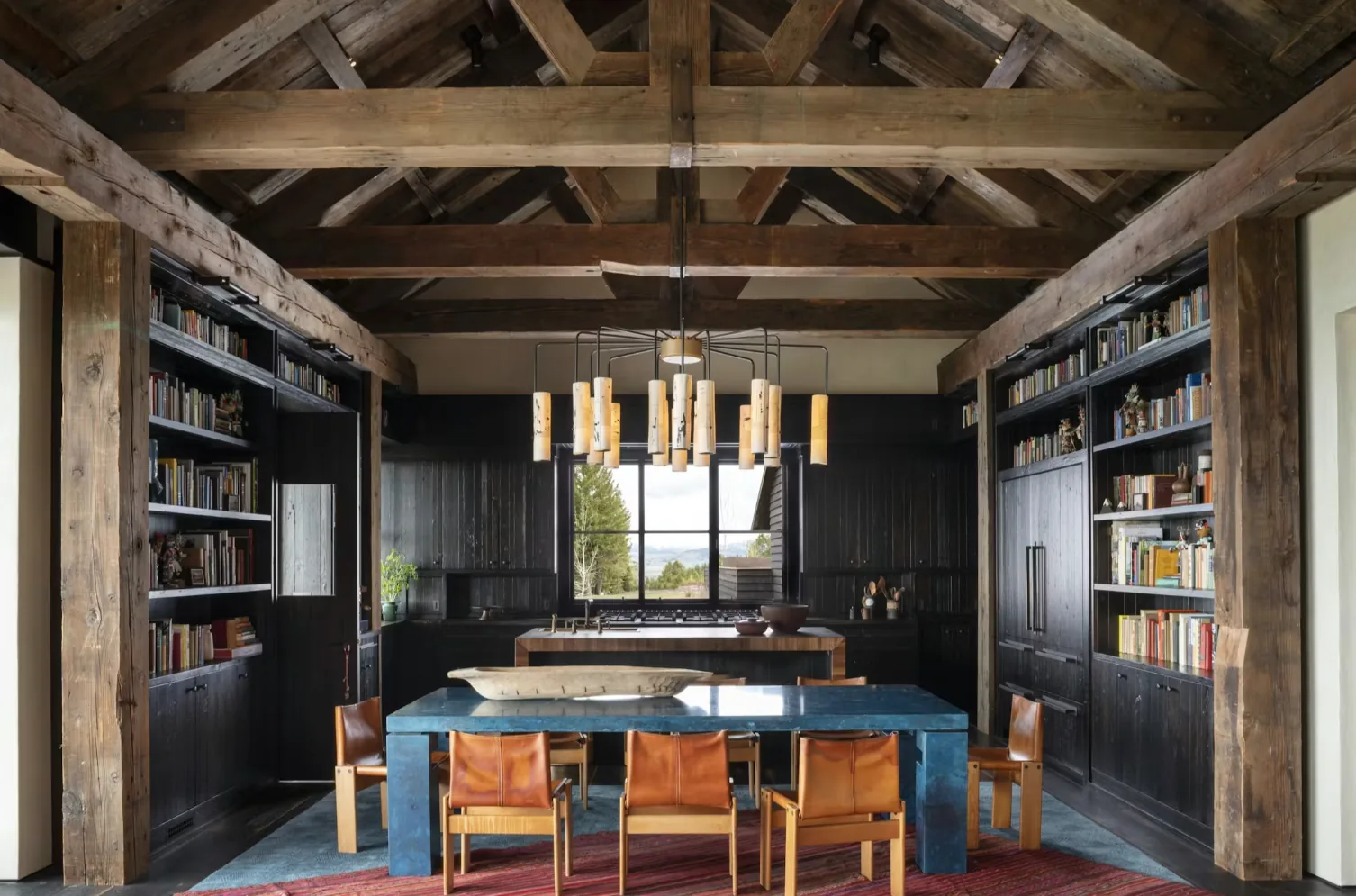 Camp Teton dining and kitchen area features exposed wood beams and a modern chandelier by Andersson Wise Architects.