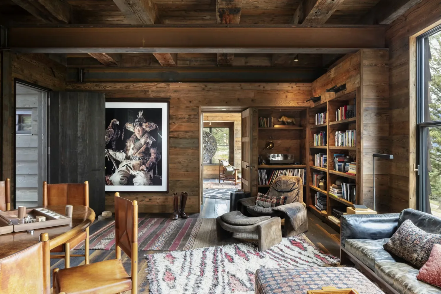 Rustic living room with wood walls, leather seating, bookcase, and a large framed artwork near the doorway.