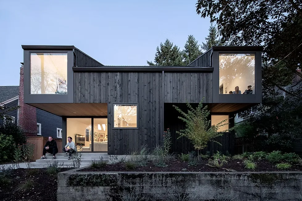 This modern house features dark vertical wood siding and distinctive large corner windows on the upper floor.