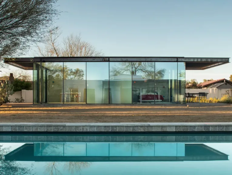 The ET Project features a flat-roofed glass house with floor-to-ceiling glazing and black window frames, reflected in a pool.