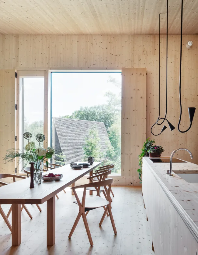 Dining space with wood-paneled walls and ceiling, a large window, and a minimalist dining table with chairs.