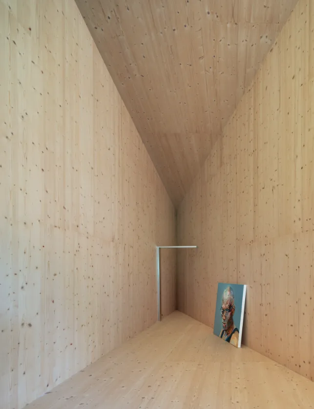 Interior view of a narrow wood-paneled corridor with a sloped ceiling and a portrait resting on the floor.