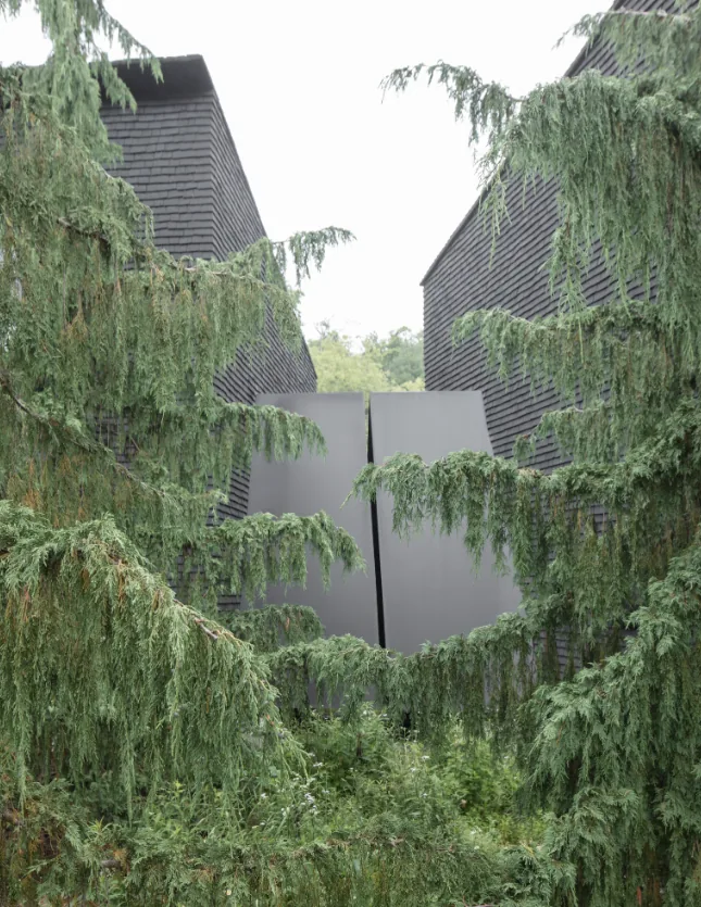 Dark shingle siding with a black metal gate framed by dense greenery at Hudson Valley House II.