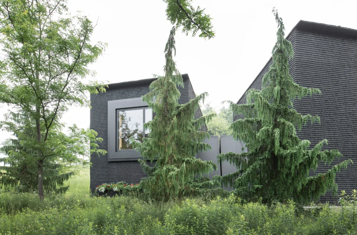 The Hudson Valley House II features dark shingle siding with large black-framed recessed windows and lush landscaping.