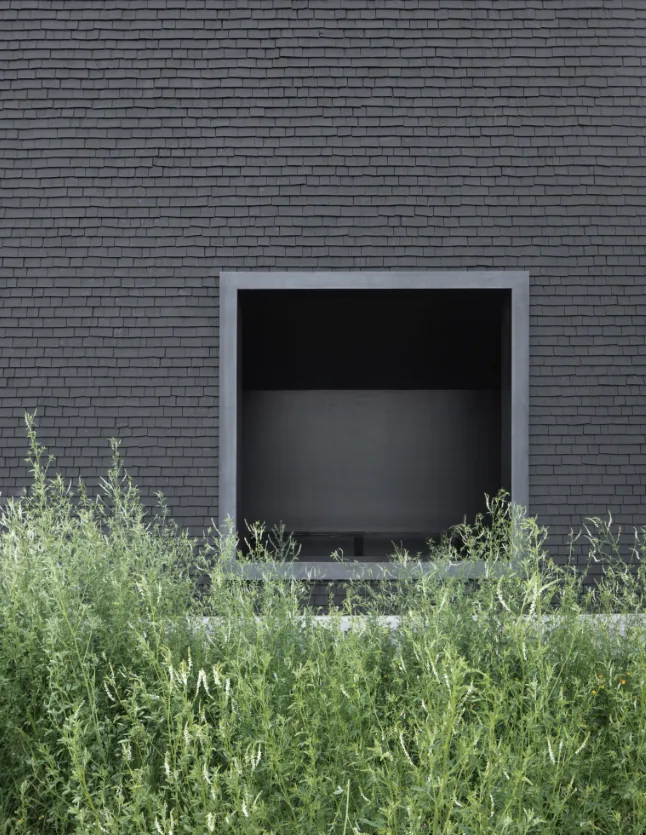 Dark shingle siding forms the exterior wall with a recessed square window opening at Hudson Valley House II.