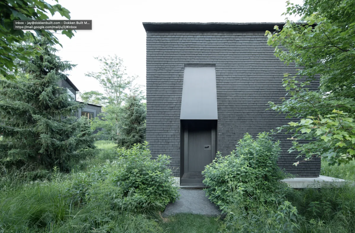 The Hudson Valley House II features black shingle siding and a recessed entrance, set amidst dense greenery in New York.