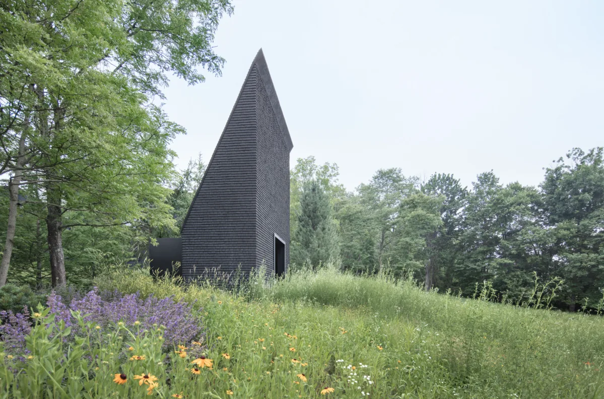 Hudson Valley House II features a steeply pitched shingle exterior blending with wild grass and trees in New York.