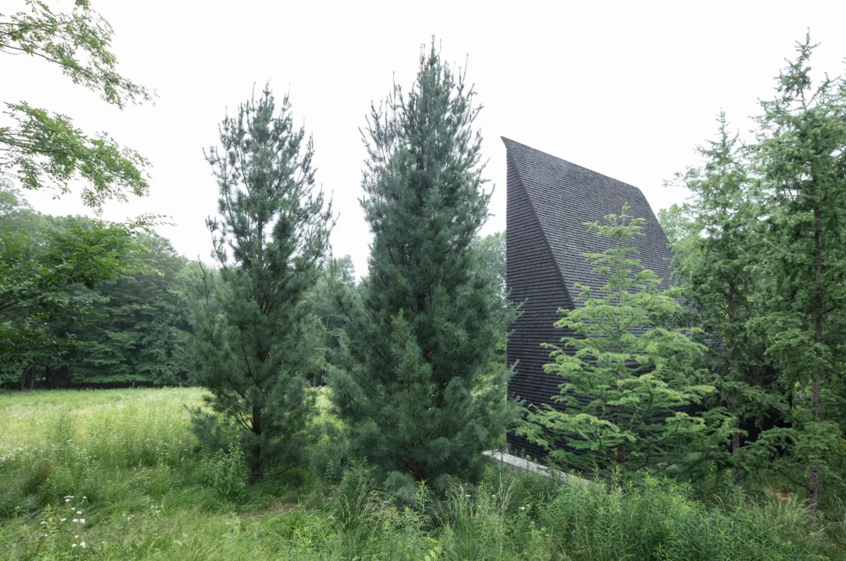 Hudson Valley House II features a dark shingle facade and steep roof, set within dense greenery and pine trees.