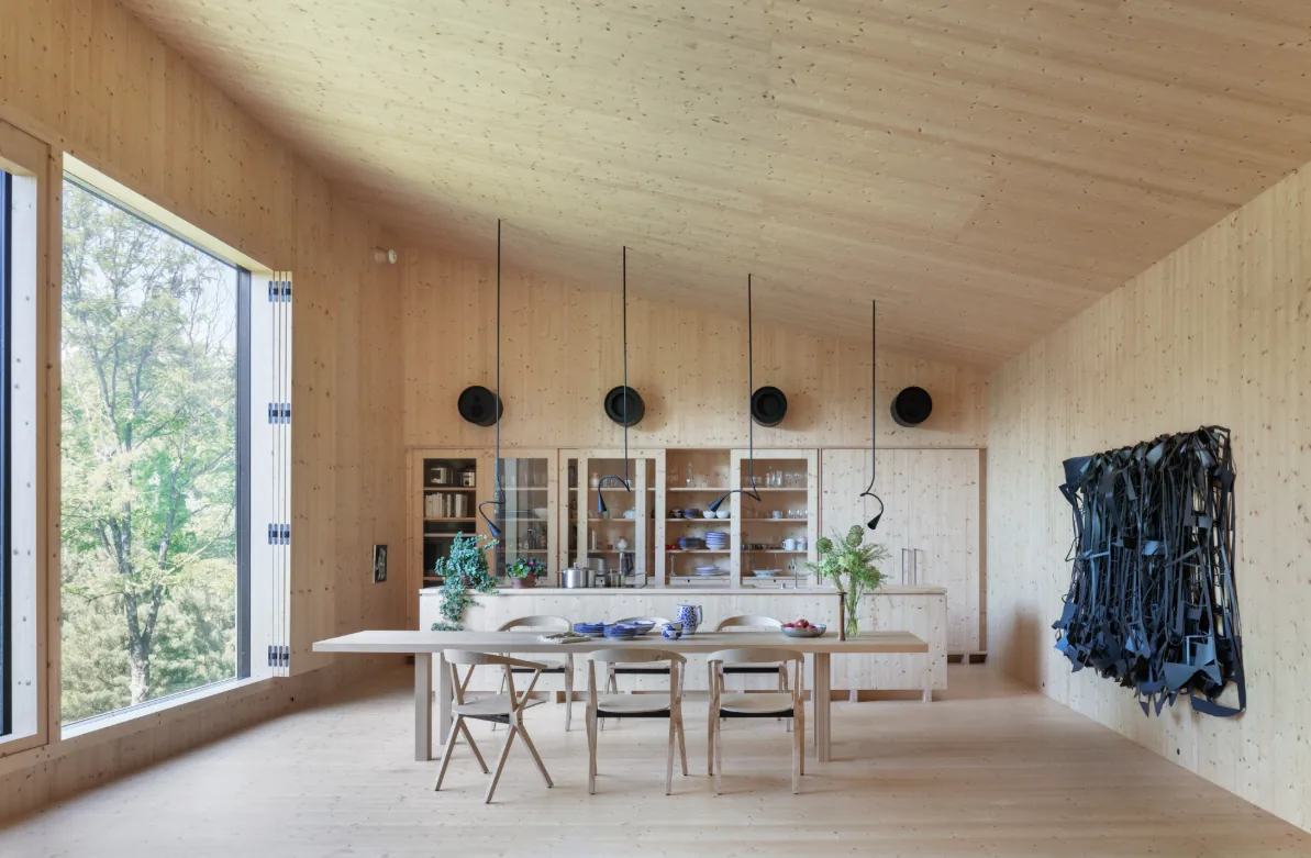 Dining space with wood walls and ceiling, large window, black pendant lights, and a sculptural wall installation.