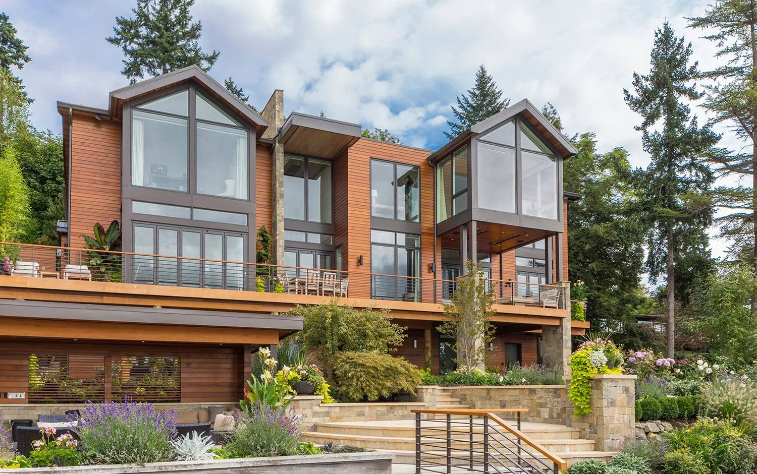Modern multi-level home with wood siding, large glass windows, and landscaped outdoor terrace in Seattle by HhLodesign.