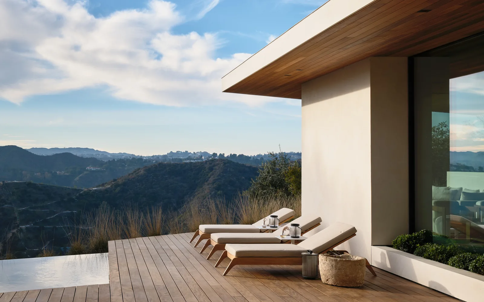 Outdoor wooden deck with lounge chairs and planted beds overlooking hills at Carla Ridge House by Montalba Architects.