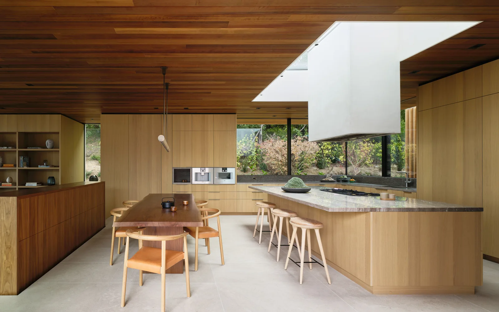 Wood-paneled kitchen and dining space in Carla Ridge House by Montalba Architects, featuring large windows and a central island.