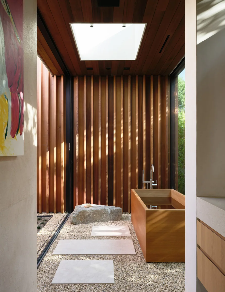 The glass-enclosed courtyard features a wooden soaking tub, vertical wood slats, and a large skylight that illuminates the space.