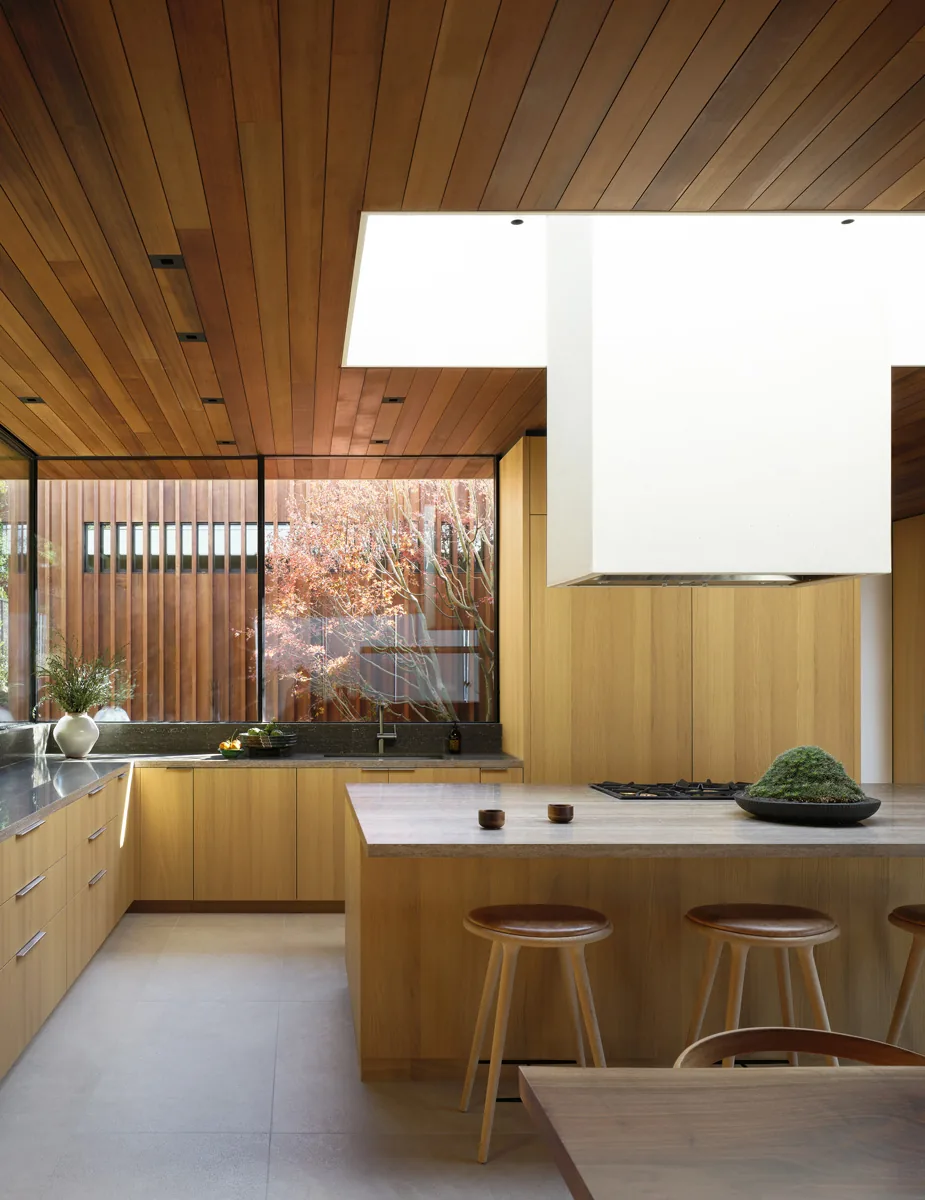 Kitchen of Carla Ridge House by Montalba Architects features wood-paneled ceiling and cabinetry with a large window showing vertical wood slats outside.