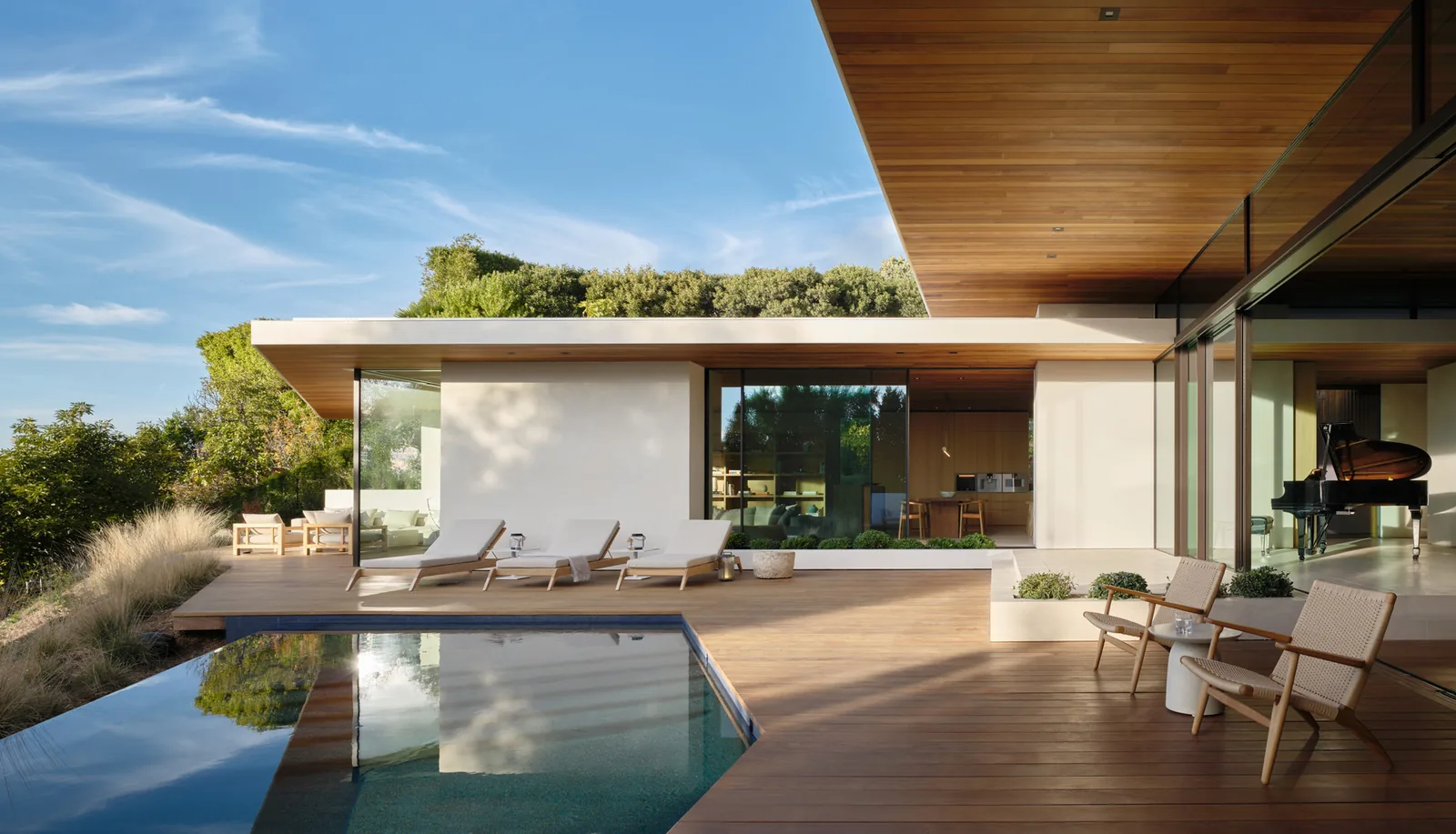 Carla Ridge House features a wooden deck poolside with lounge chairs and a seamless indoor-outdoor transition through glass sliding doors.