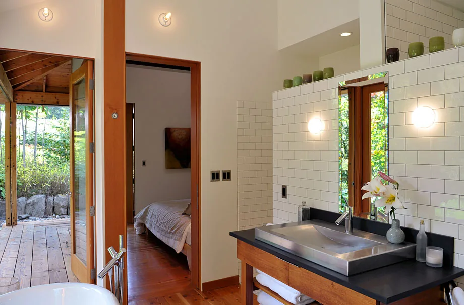 Bathroom with a wooden vanity, stainless steel sink, tile backsplash, and views through a bedroom and covered porch.