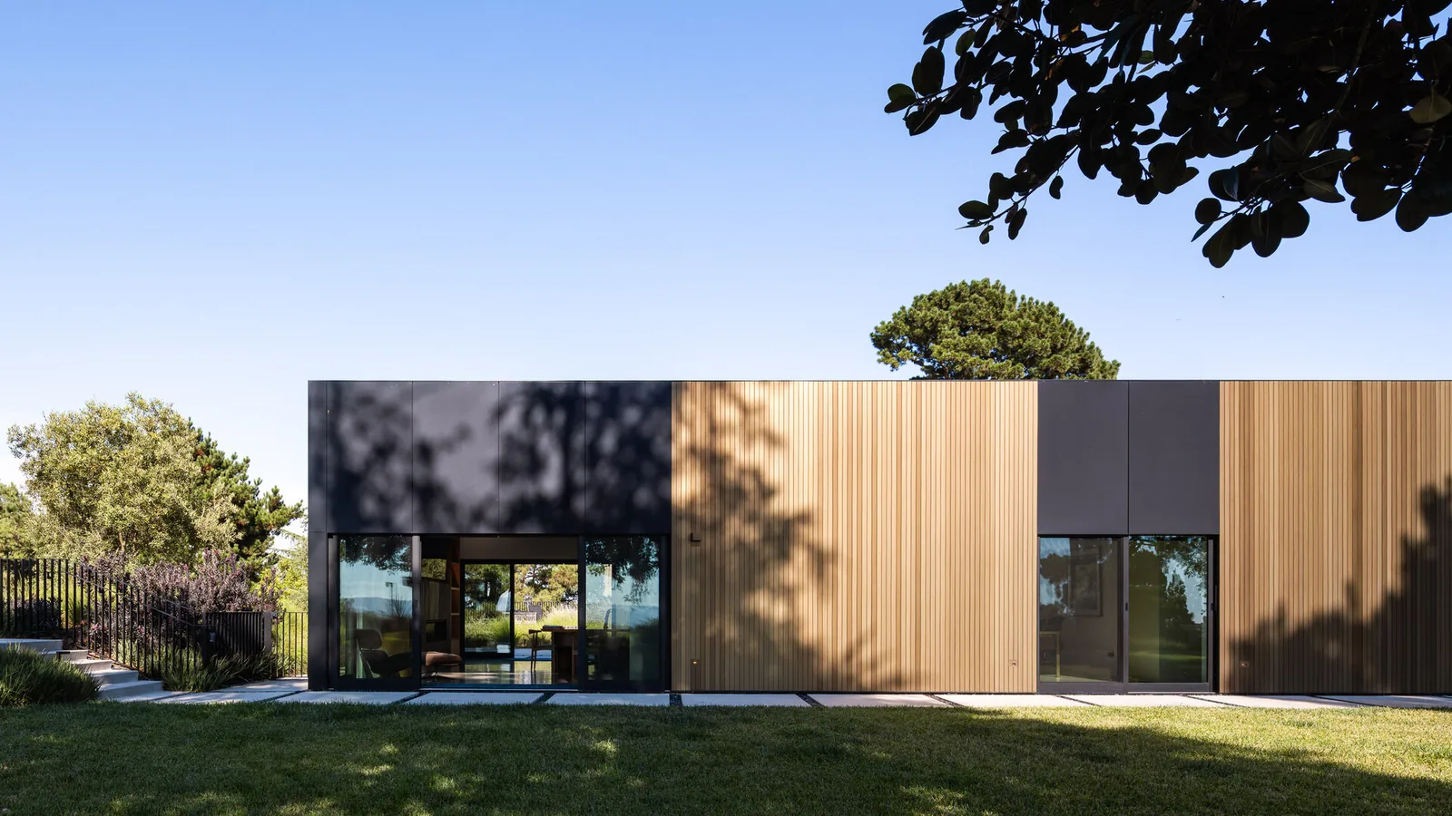 The Bronze and Black House features a modern exterior with large glass doors and a combination of vertical wood panels and black cladding.