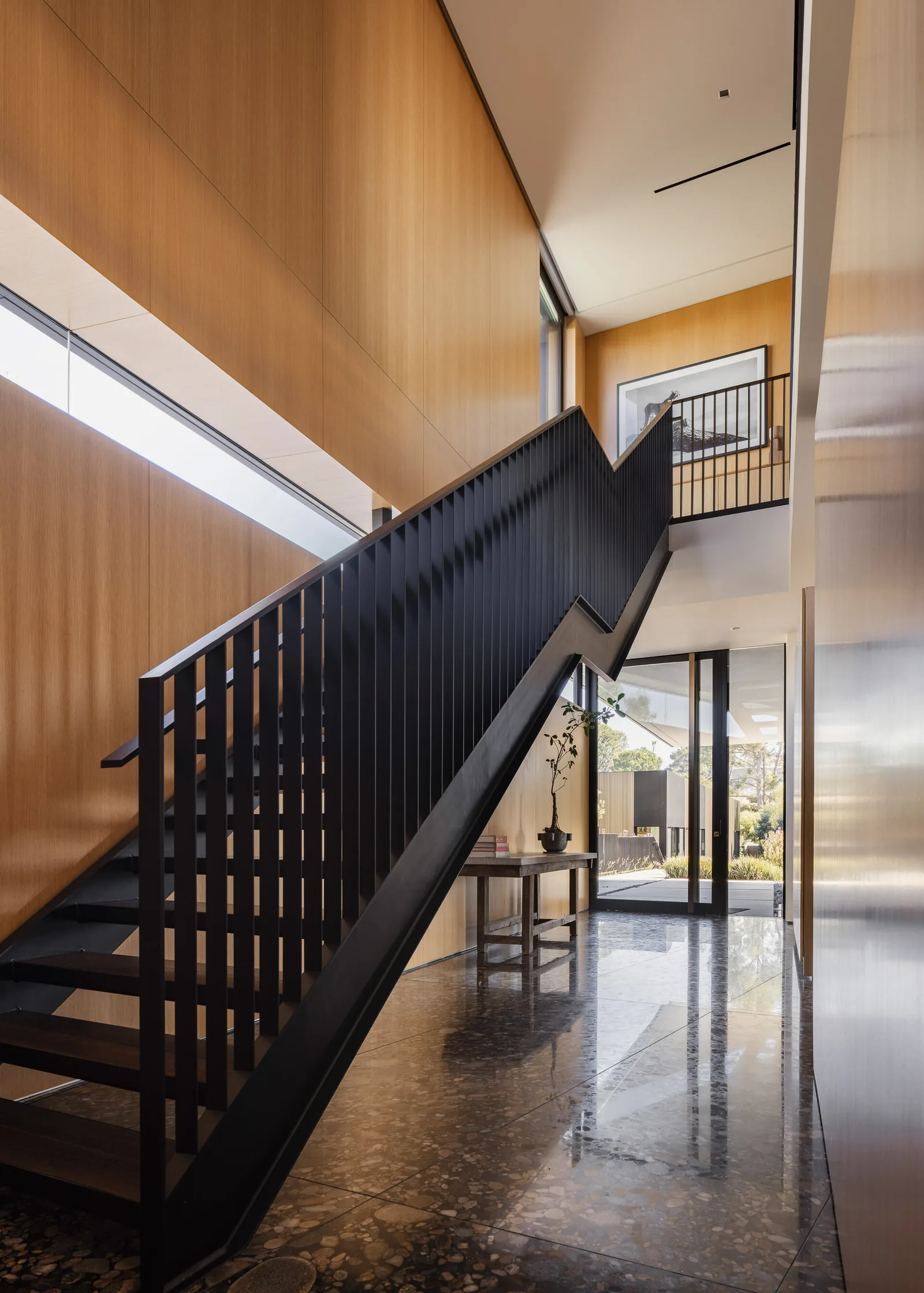 Modern stairway with black railing contrasted against wood-paneled walls and polished stone flooring under natural light.