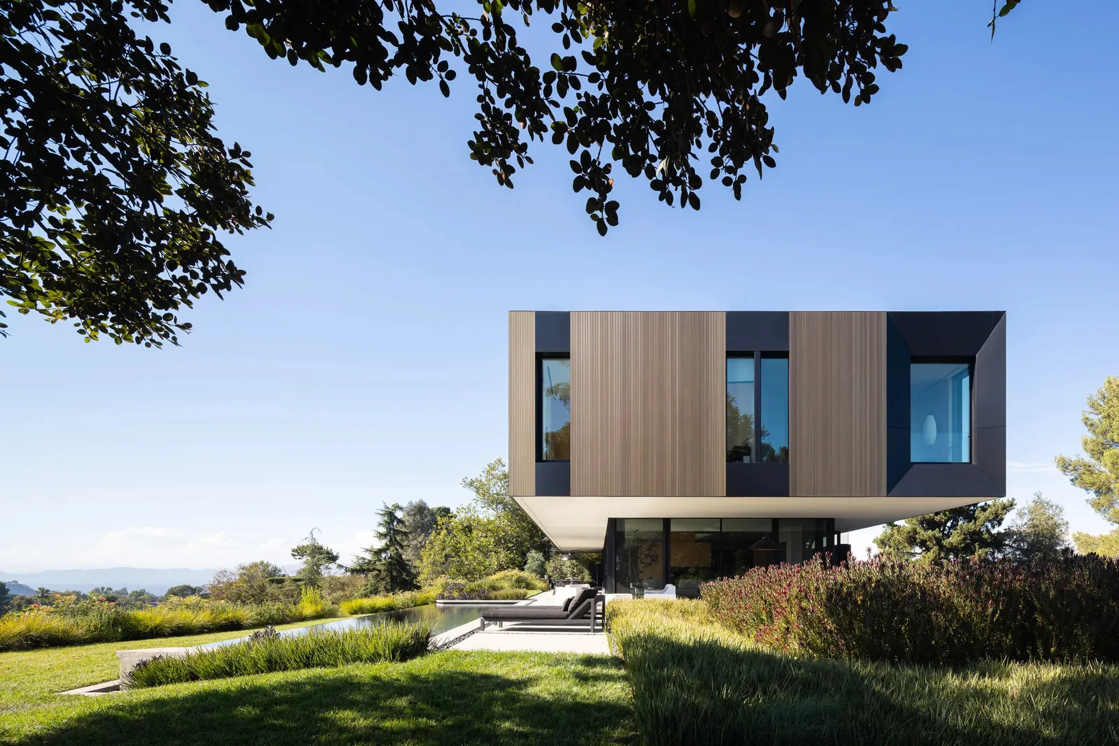 The Bronze and Black House by SPF:architects showcases an upper floor with bronze vertical panels and black framed windows over a glass-encased ground floor.
