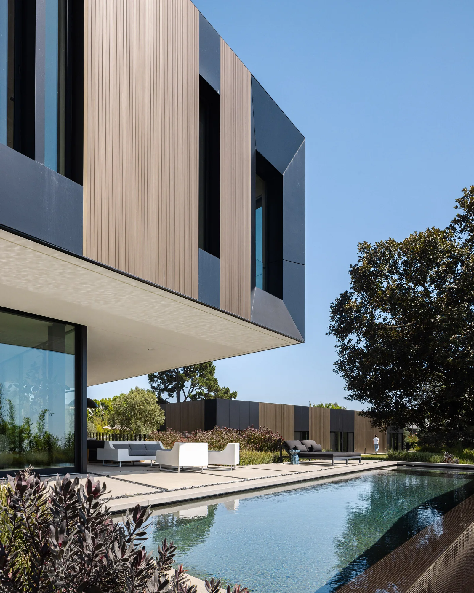 The Bronze and Black House features vertical wood panels, black window frames, and a reflecting pool with outdoor seating.