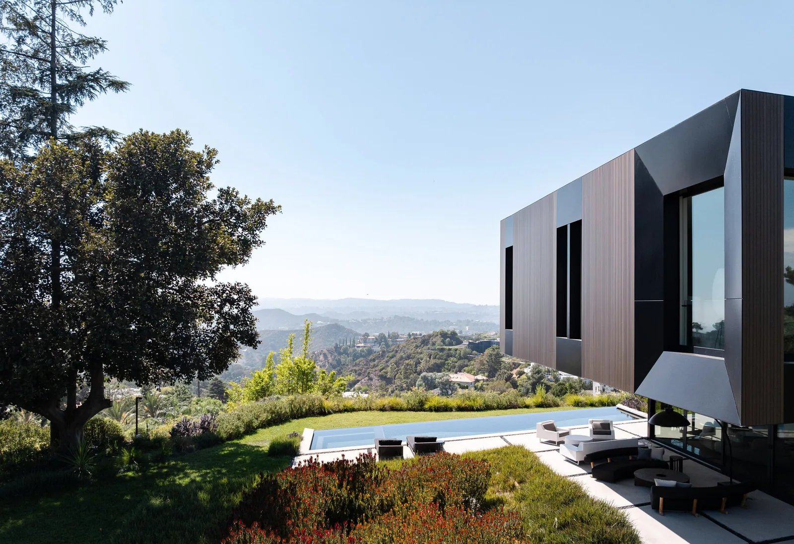 The Bronze and Black House by SPF:architects features vertical wood paneling and black metal cladding with large glass doors opening to an outdoor living area and pool.