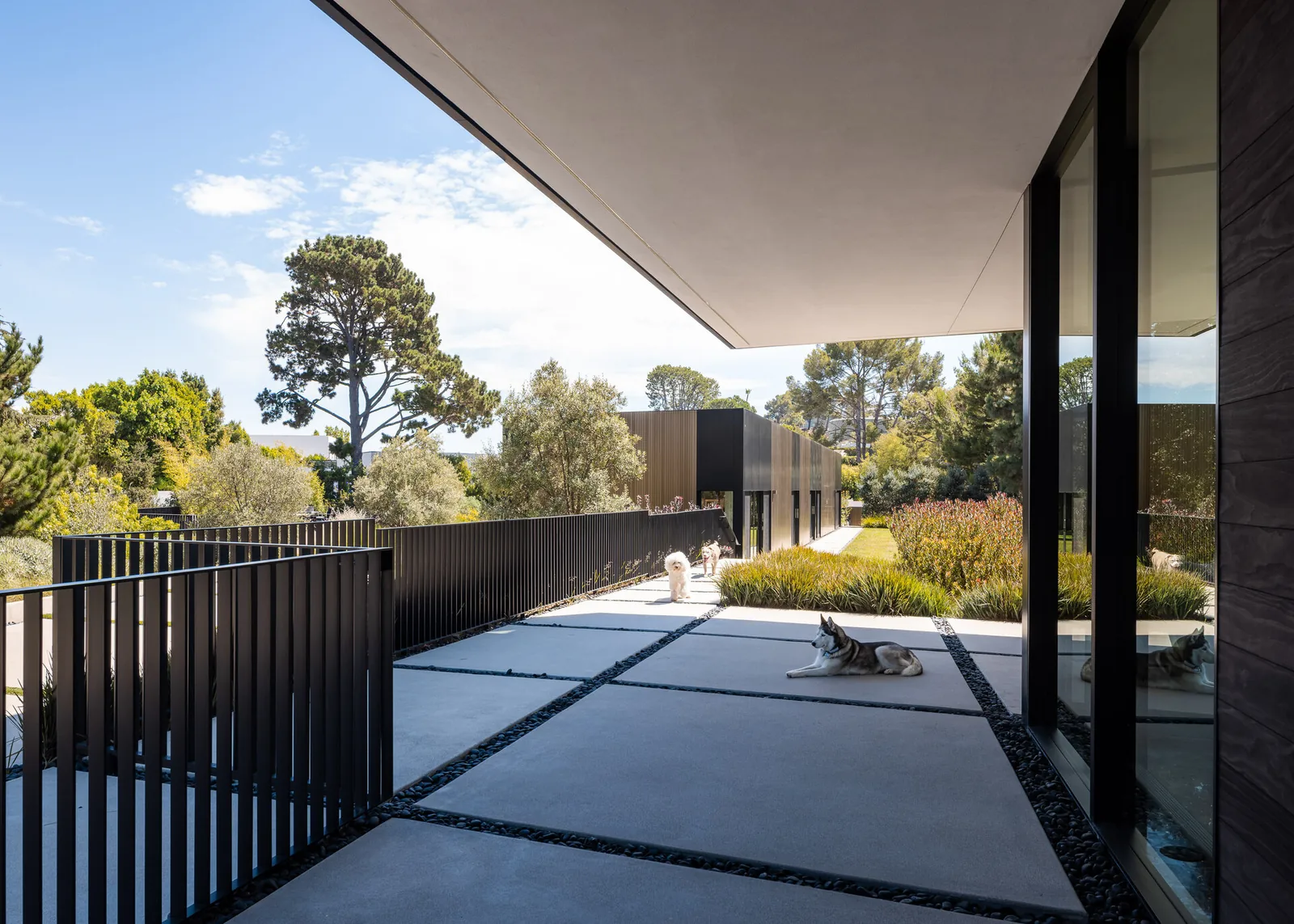 The Bronze and Black House features a sleek patio with large concrete slabs, black railings, and glass walls overlooking landscaped greenery.