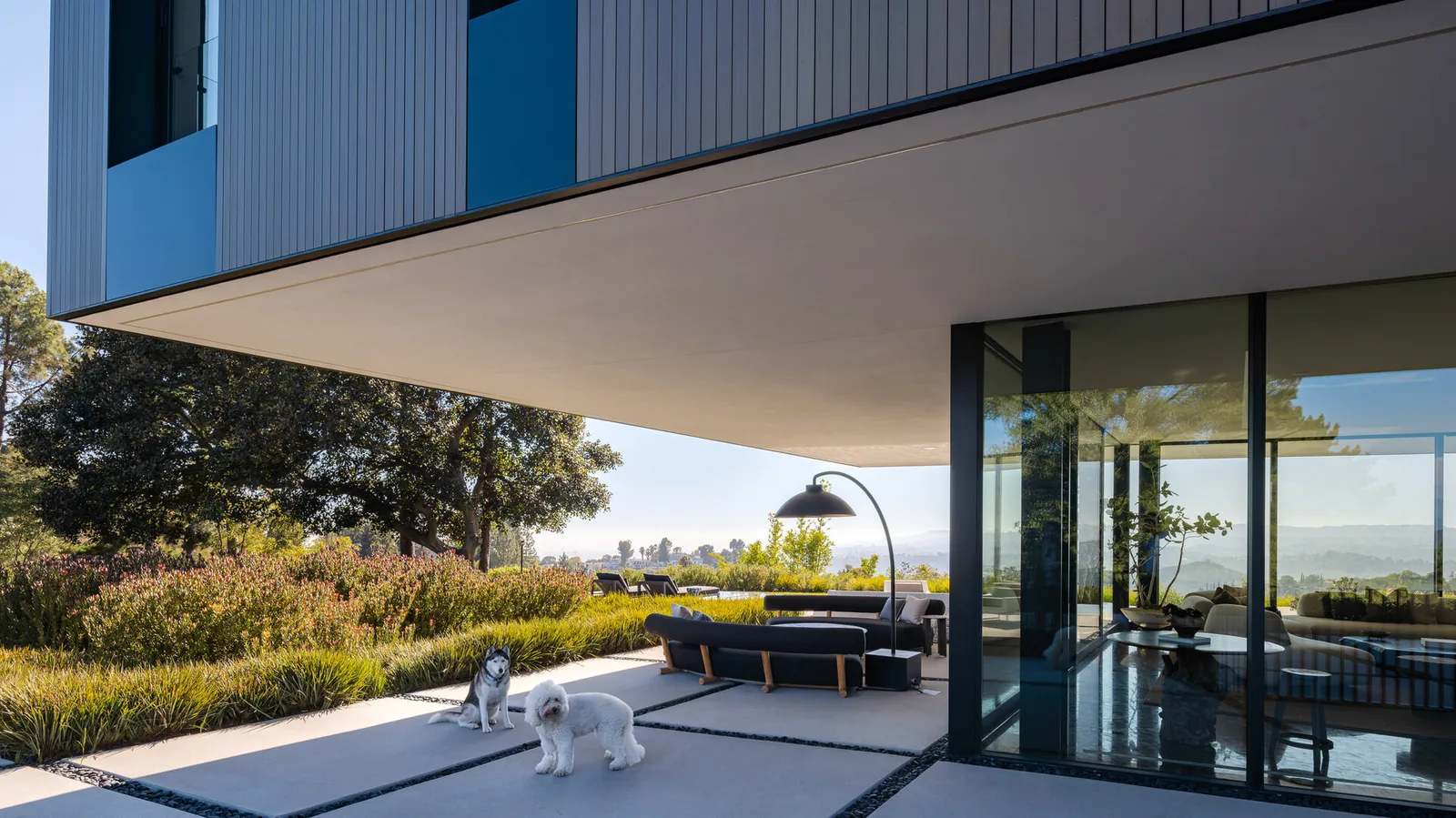 The Bronze and Black House features vertical wood paneling and large windows behind a covered patio with outdoor furniture.